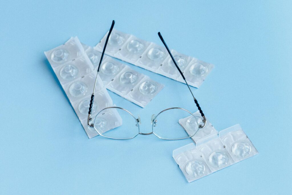 Eyeglasses and sealed contact lenses on a soft blue surface, representing vision care.